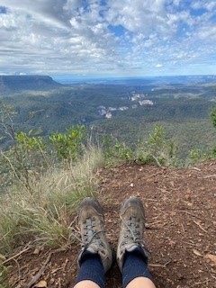 A photo of a persons legs with hiking boots seated at the top of the Gorge looking over the scenery.